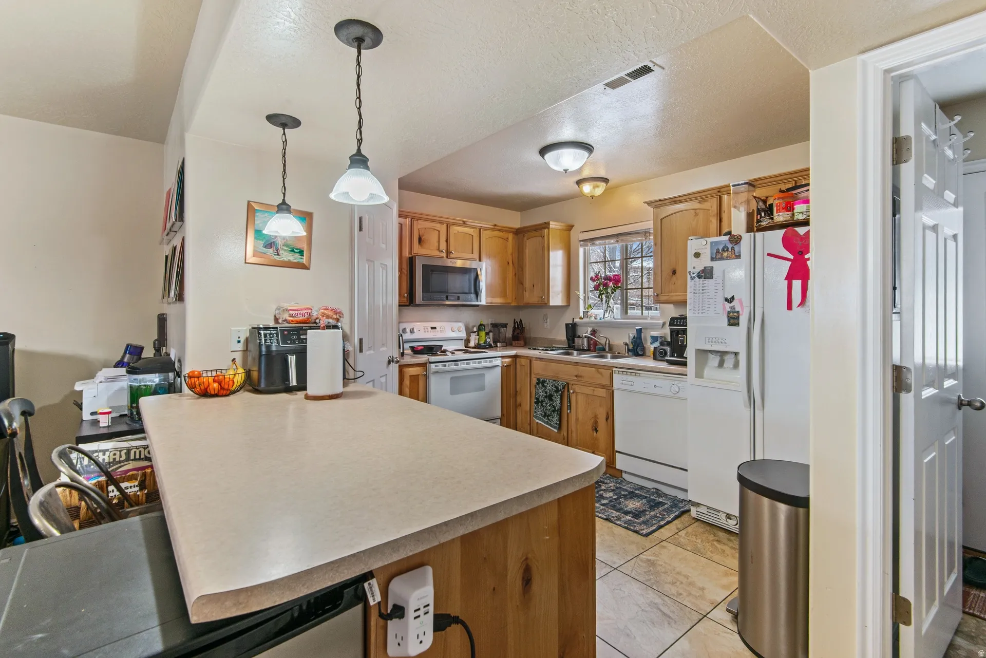 Kitchen with a peninsula, white appliances, light countertops, hanging light fixtures, and a textured ceiling
