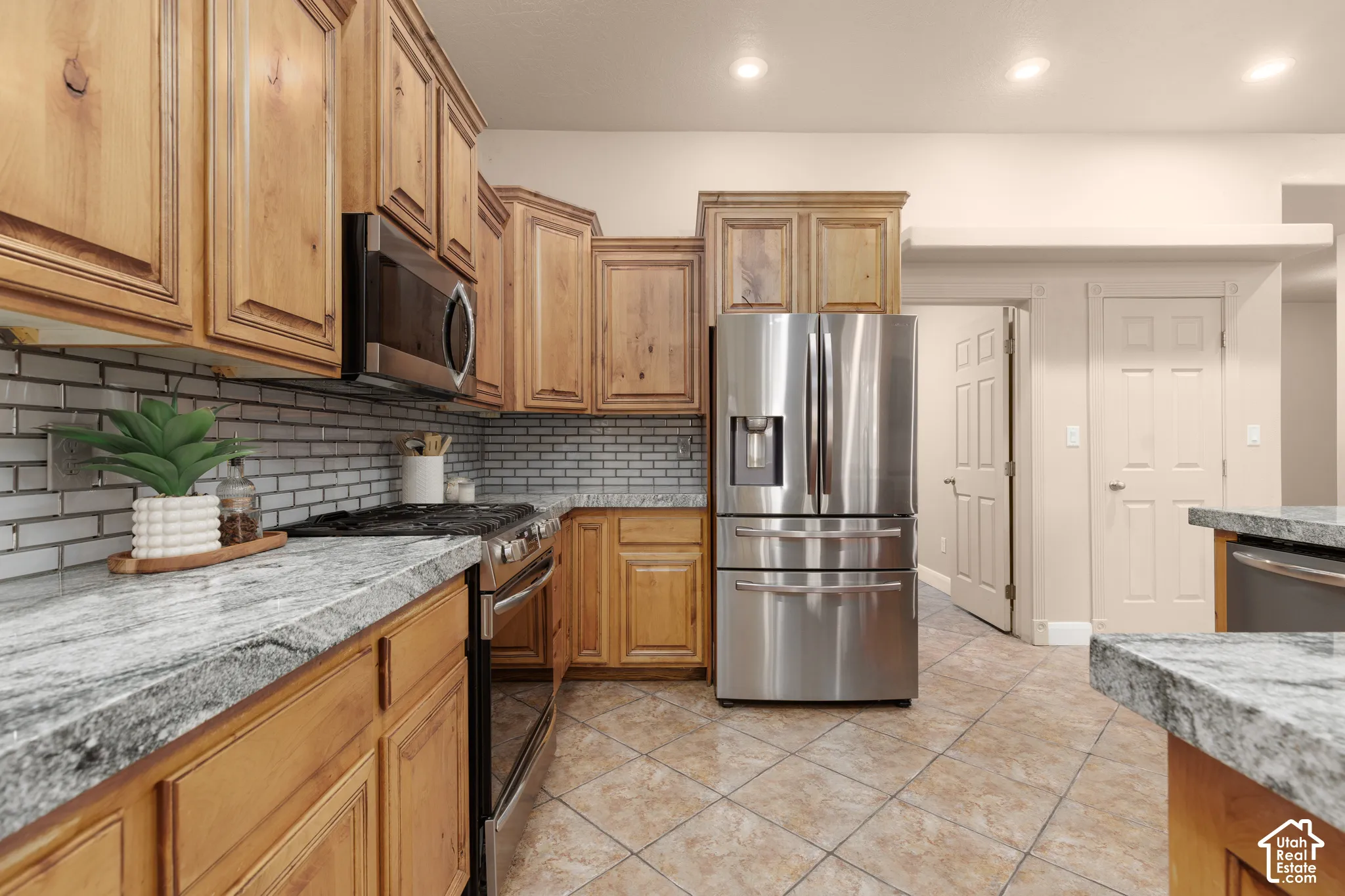 Kitchen with stainless steel appliances, light tile patterned floors, recessed lighting, tasteful backsplash, and light stone counters