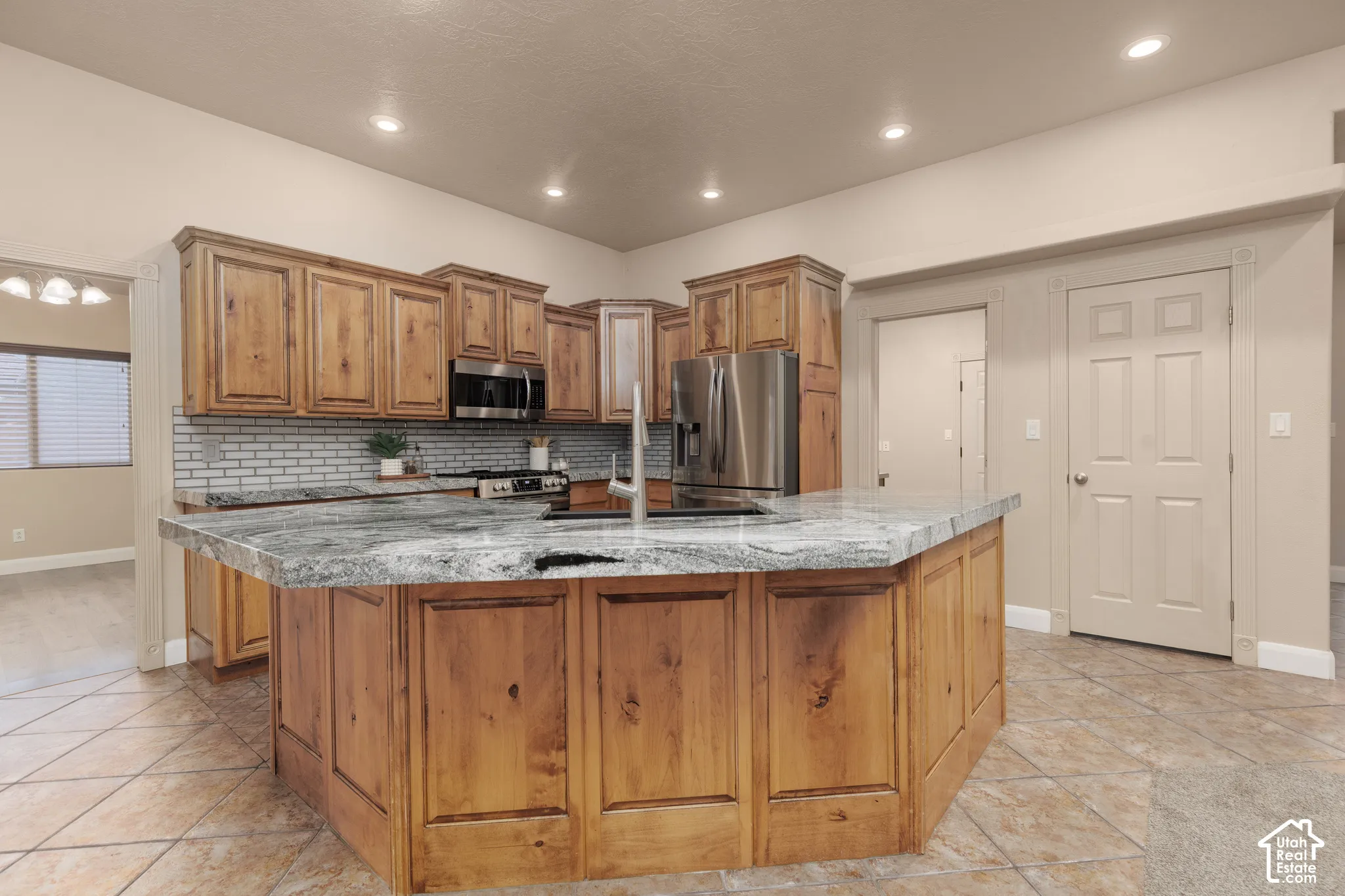 Kitchen featuring wood finish cabinetry, stainless steel appliances, a large island, light tile patterned floors, and light stone countertops