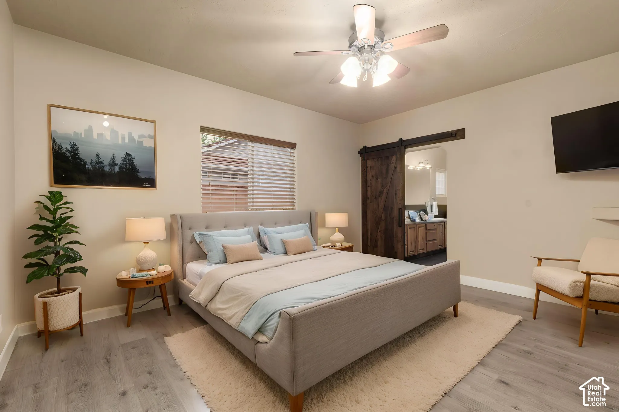 Primary Suite featuring a barn door, light wood finished floors, a ceiling fan, and connected bathroom, AI staging