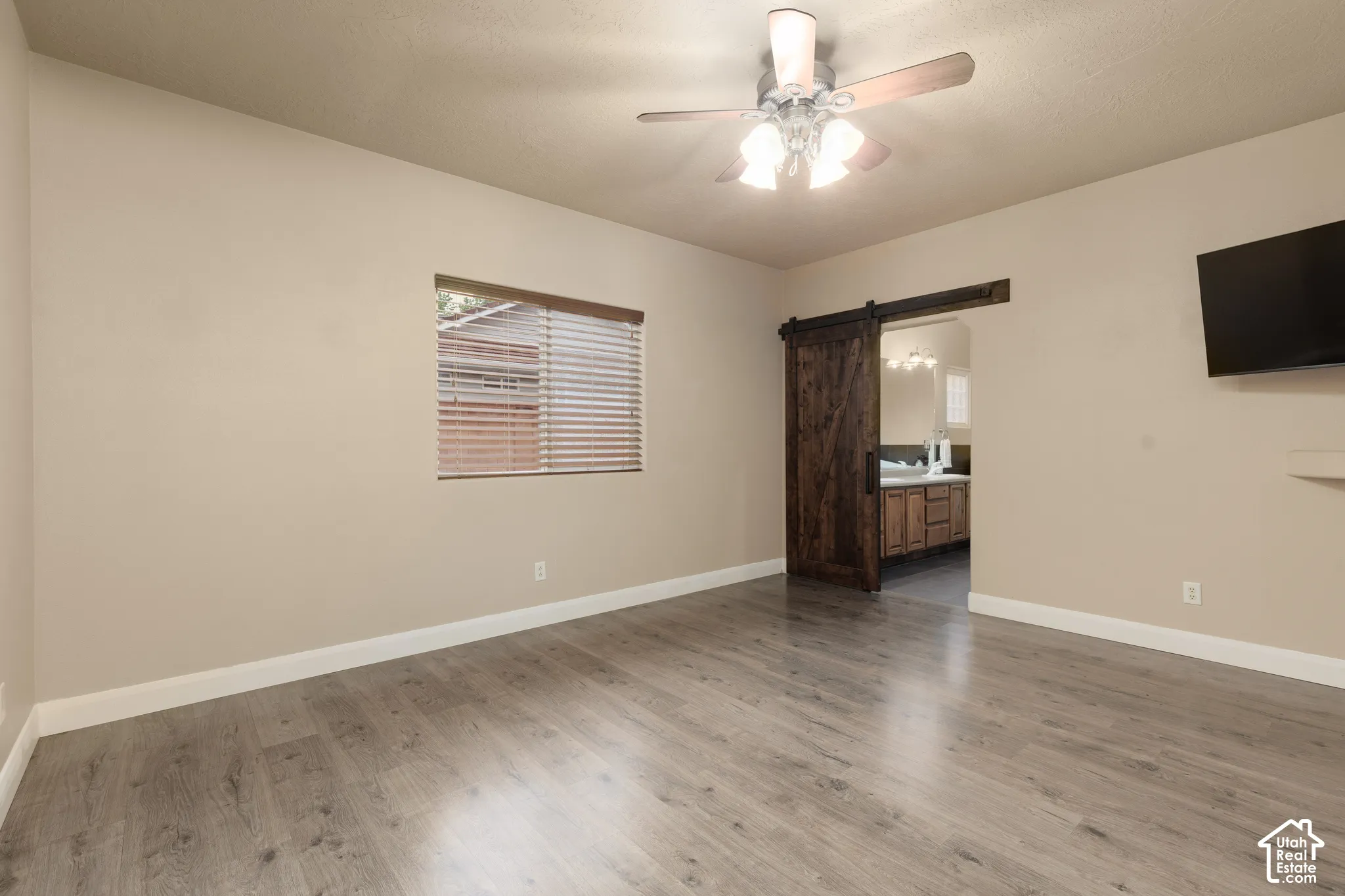 Primary suite featuring a barn door, light wood finished floors, a ceiling fan, and ensuite bathroom