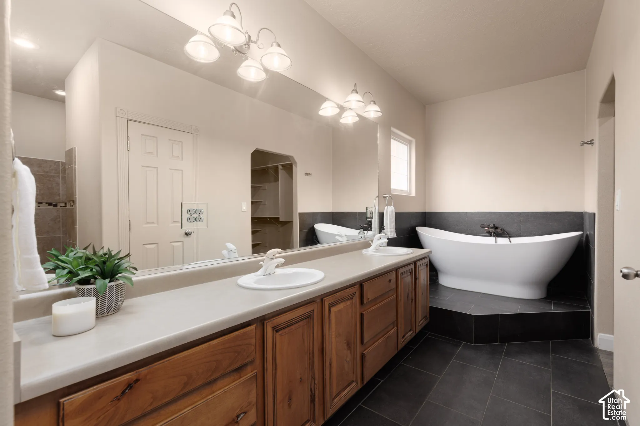 Primary bath featuring double vanity, dark tile patterned flooring, tile walls, a soaking tub, and a walk in shower