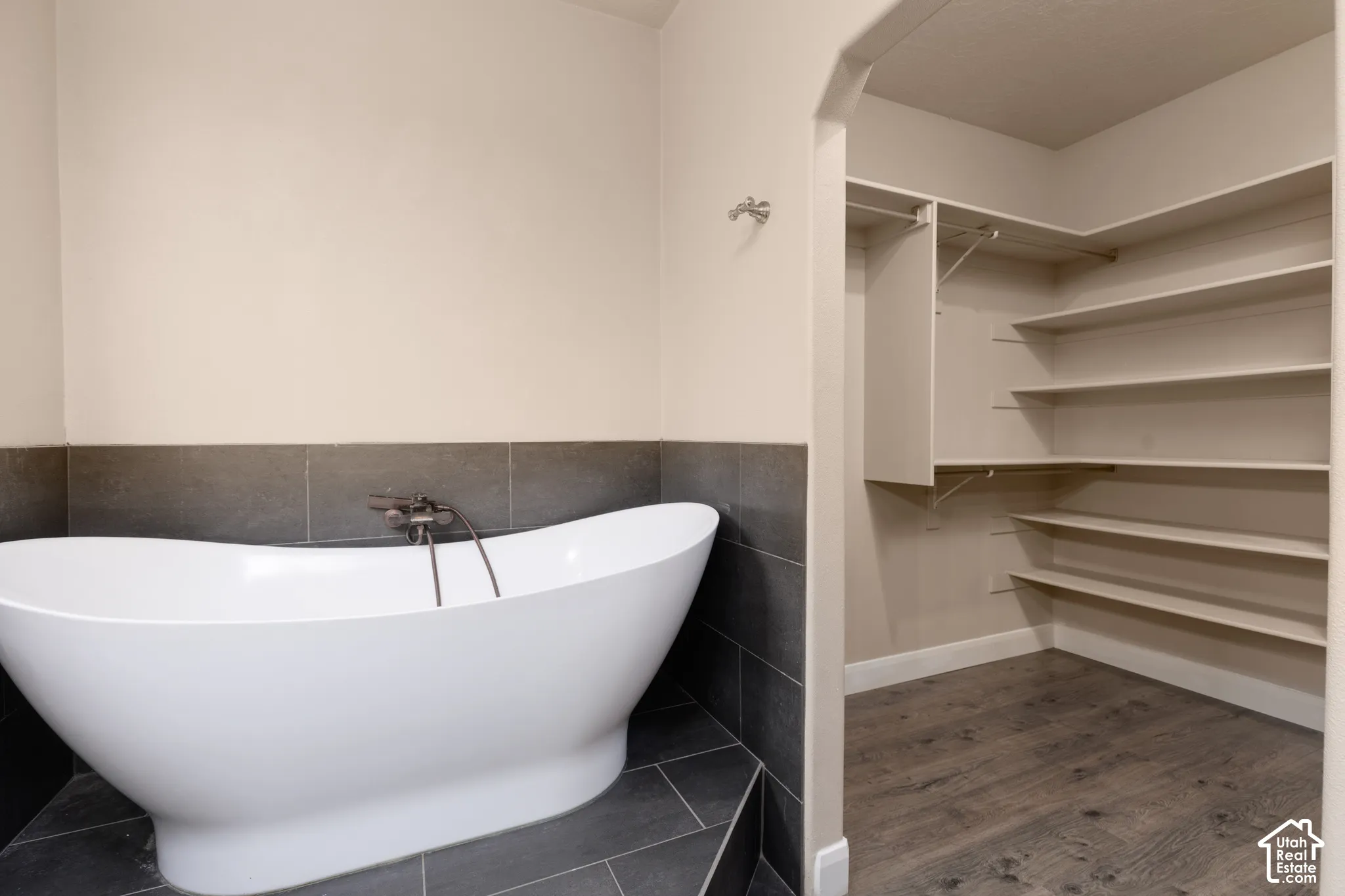 Primary bathroom with  wood-style floors, tile walls, a freestanding tub, and private stool