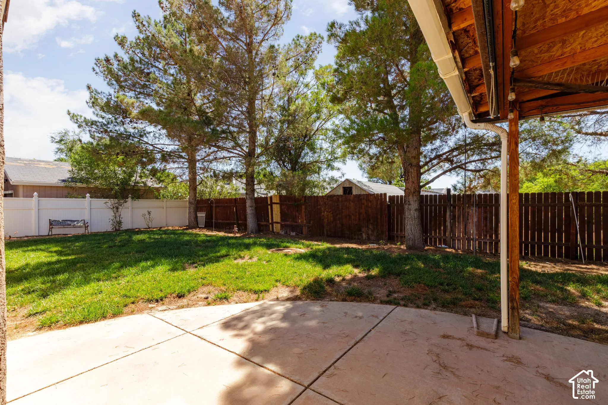 Concrete patio with an overhead wood-finish structure, overlooking a grass yard with mature trees
