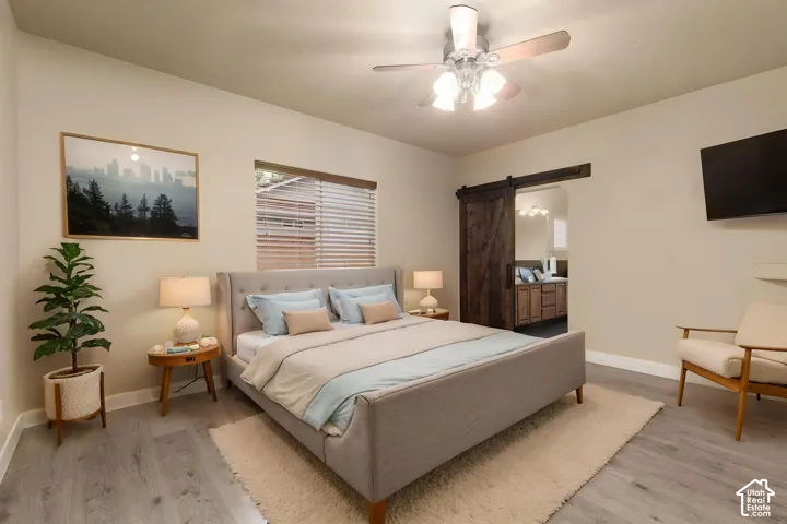 Primary Suite featuring a barn door, light wood finished floors, a ceiling fan, and connected bathroom, AI staging
