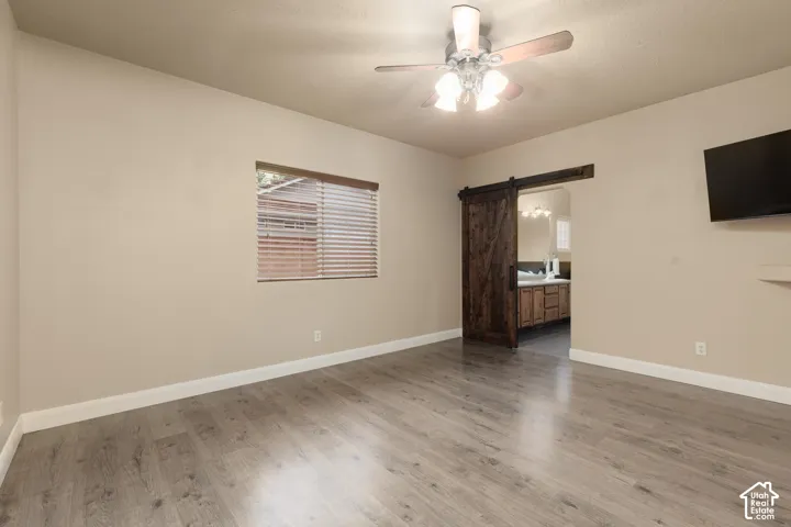 Primary suite featuring a barn door, light wood finished floors, a ceiling fan, and ensuite bathroom