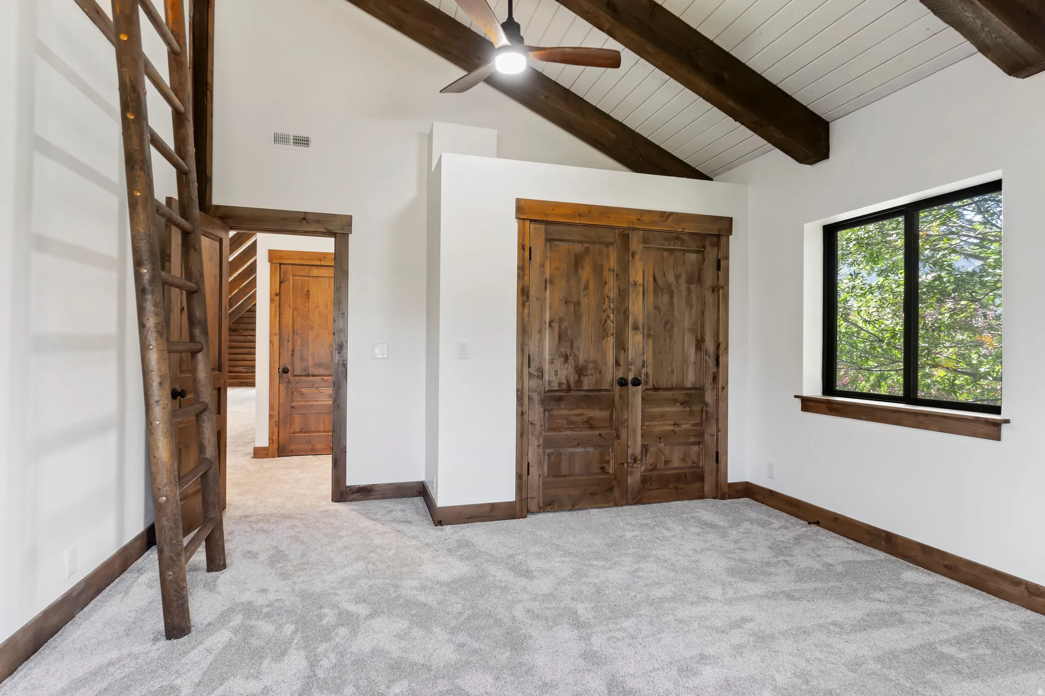 Carpeted bedroom with a ceiling fan, a high wood beamed ceiling, and a closet
