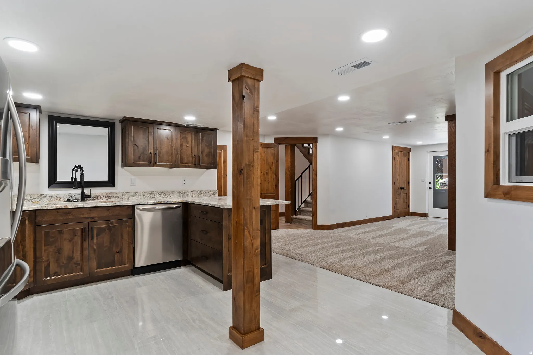 Kitchen featuring dark wood finish cabinets, stainless steel appliances, light stone counters, light carpet, and recessed lighting