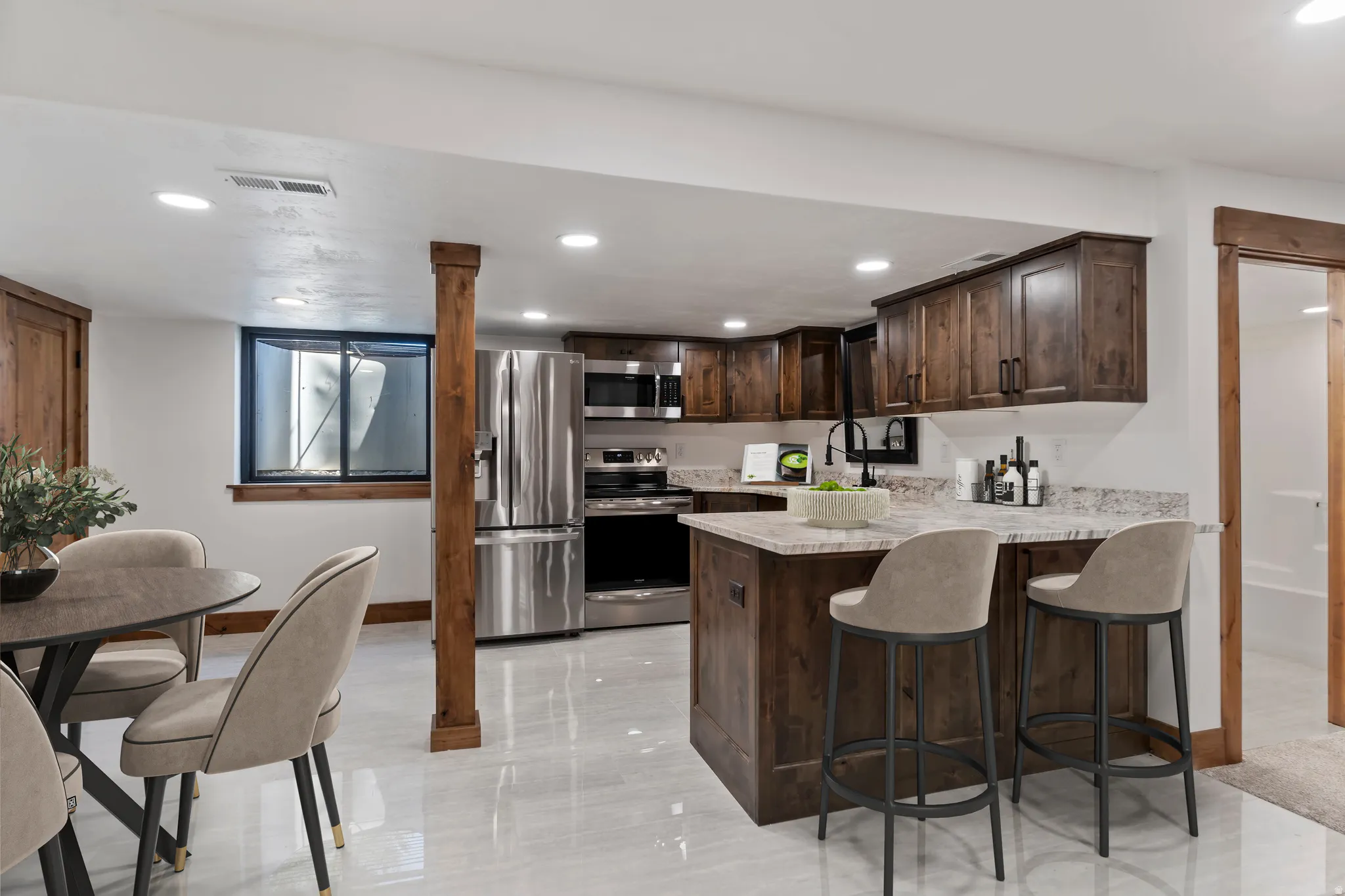 Kitchen with dark wood finish cabinetry, a peninsula, stainless steel appliances, a breakfast bar area, and light stone counters