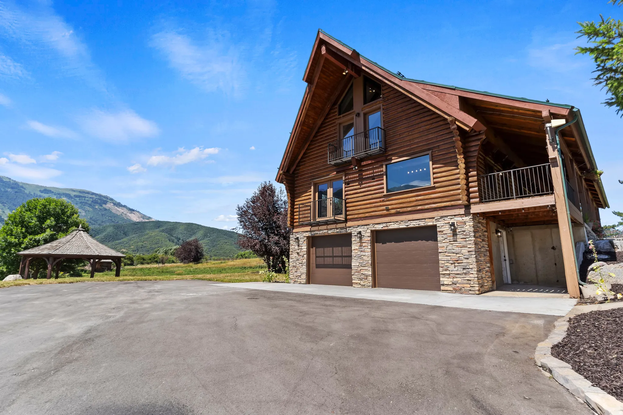View of side of home with stone siding, log siding, a mountain view, an attached garage, and a balcony