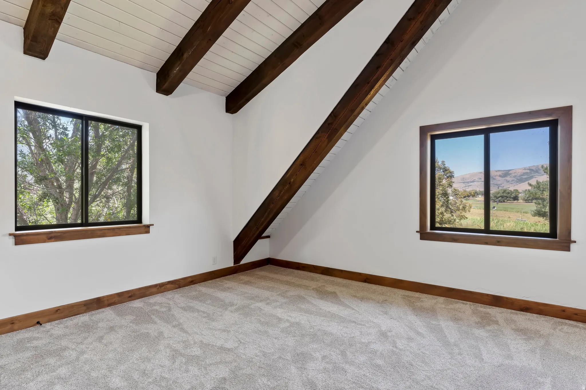 Empty room with lofted ceiling with beams, a mountain view, light colored carpet, plenty of natural light, and wooden ceiling