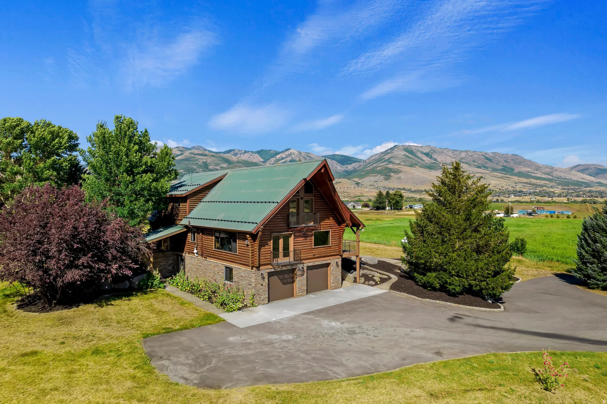 View of property exterior with a lawn, stone siding, a garage, and log exterior