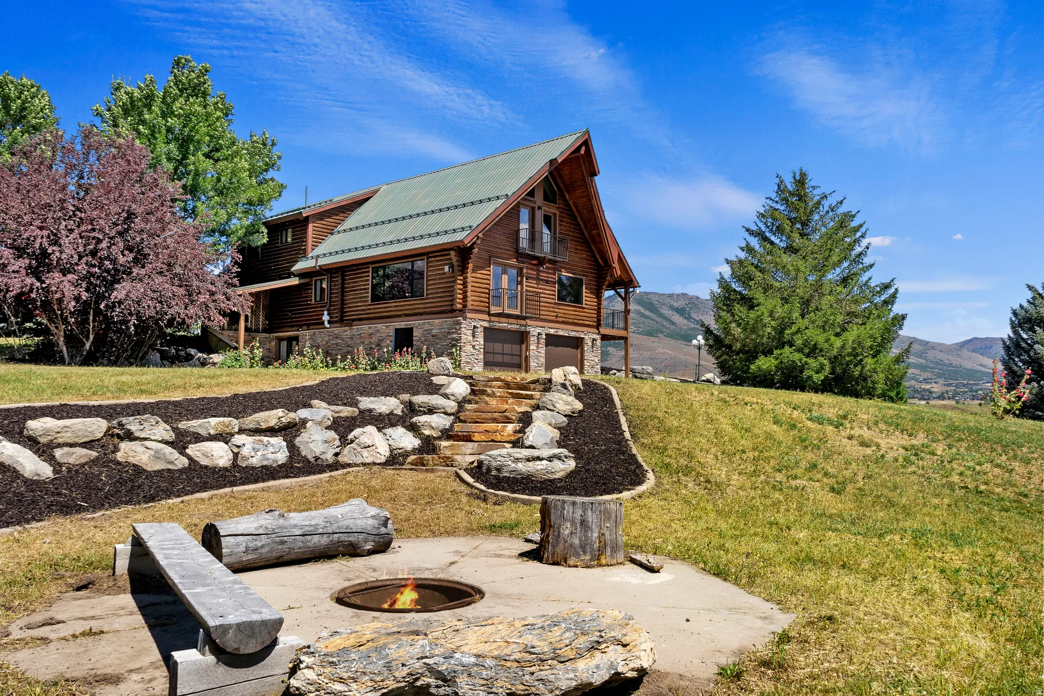 Rear view of property with a fire pit, log exterior, a yard, an attached garage, and a mountain view