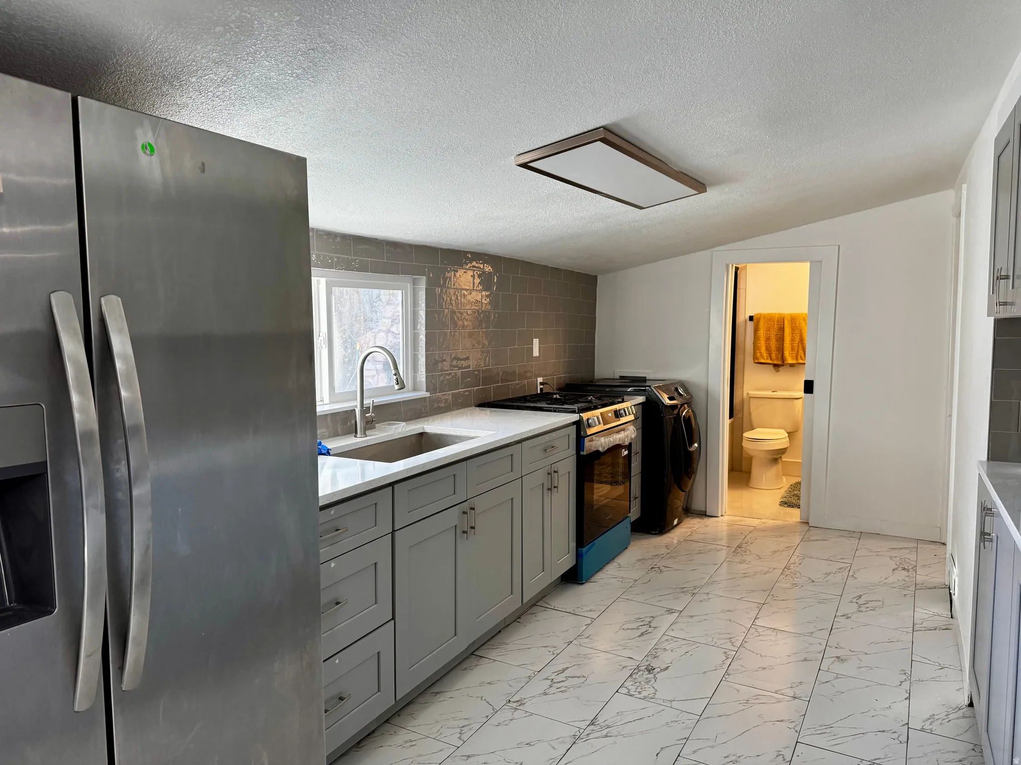 Kitchen with stainless steel refrigerator with ice dispenser, gas stove, light marble finish floors, gray cabinetry, and a textured ceiling