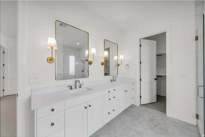 Bathroom with a marble finish shower, double vanity, a walk in closet, and light marble finish floors