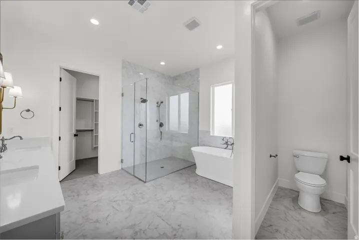 Full bath with a marble finish shower, light marble finish flooring, a spacious closet, a freestanding tub, and double vanity