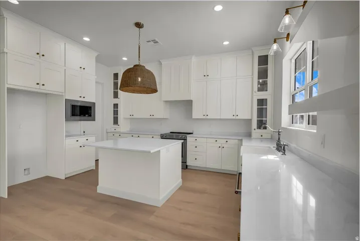 Kitchen featuring glass fronted cabinets, white cabinetry, stainless steel appliances, a kitchen island, and decorative light fixtures