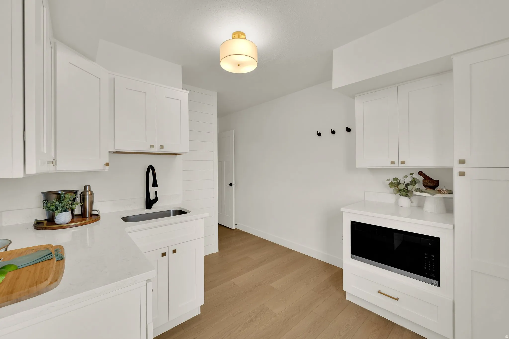 Kitchenette with white cabinets, light stone counters, light wood-style floors, and built in microwave