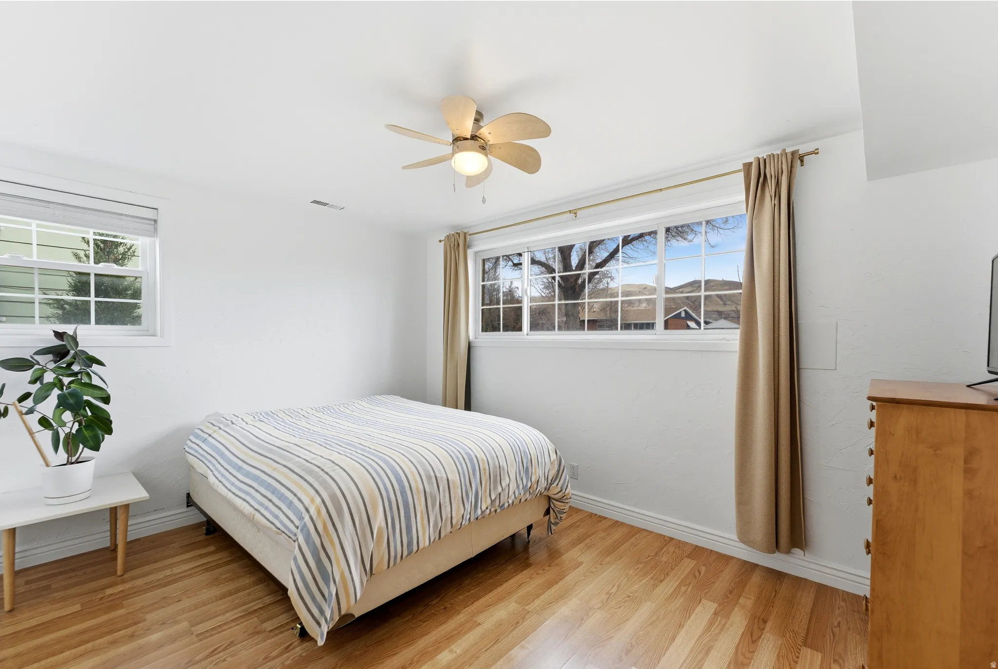 Bedroom with light wood finished floors, multiple windows, and ceiling fan