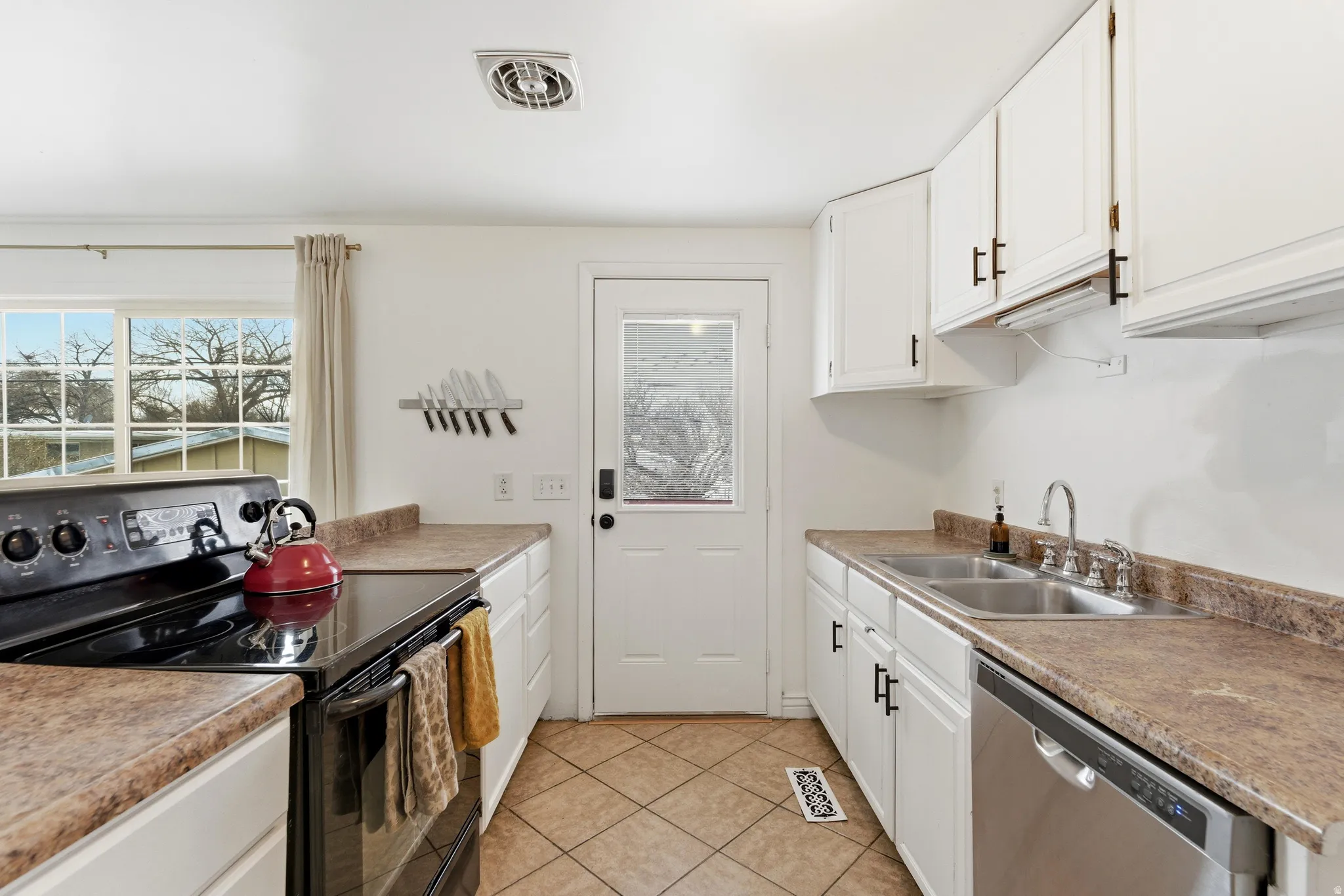 Kitchen featuring electric range, white cabinets, dishwasher, and light tile patterned floors