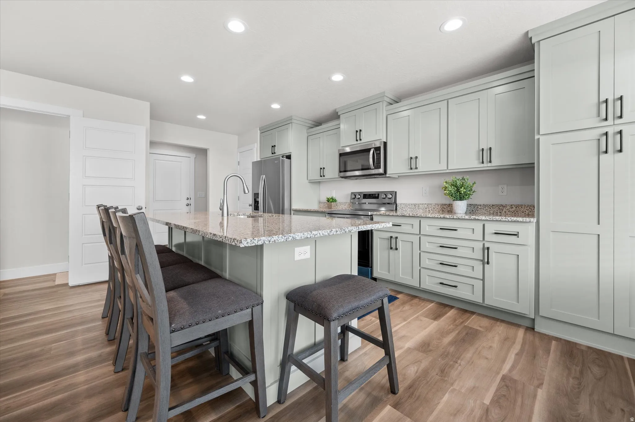 Kitchen with light stone counters, a kitchen bar, a kitchen island with sink, stainless steel appliances, and light wood-style floors