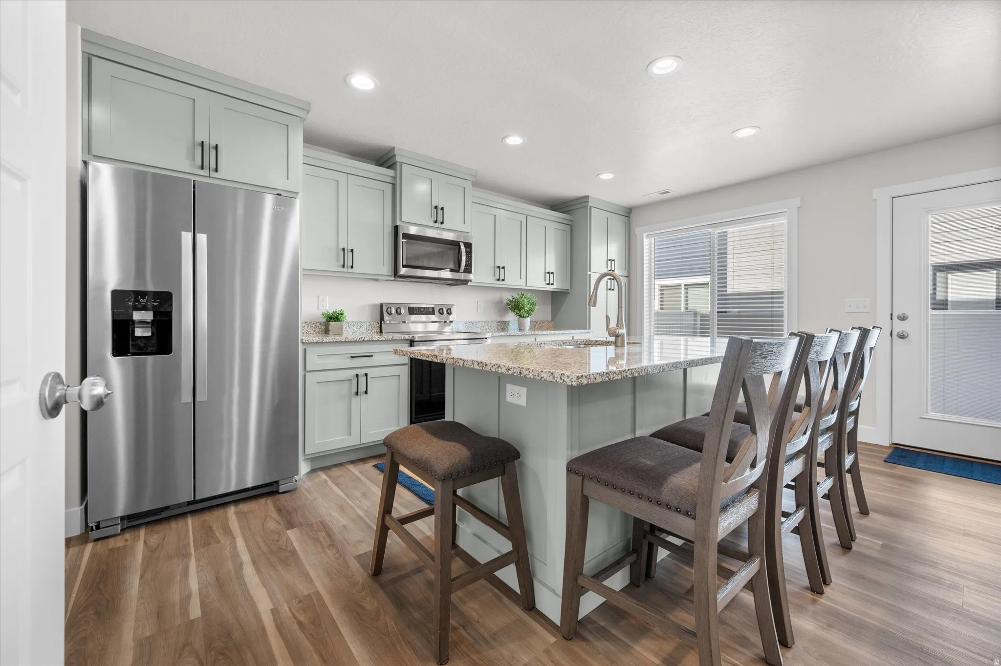 Kitchen with stainless steel appliances, light stone countertops, a breakfast bar area, light wood finished floors, and an island with sink