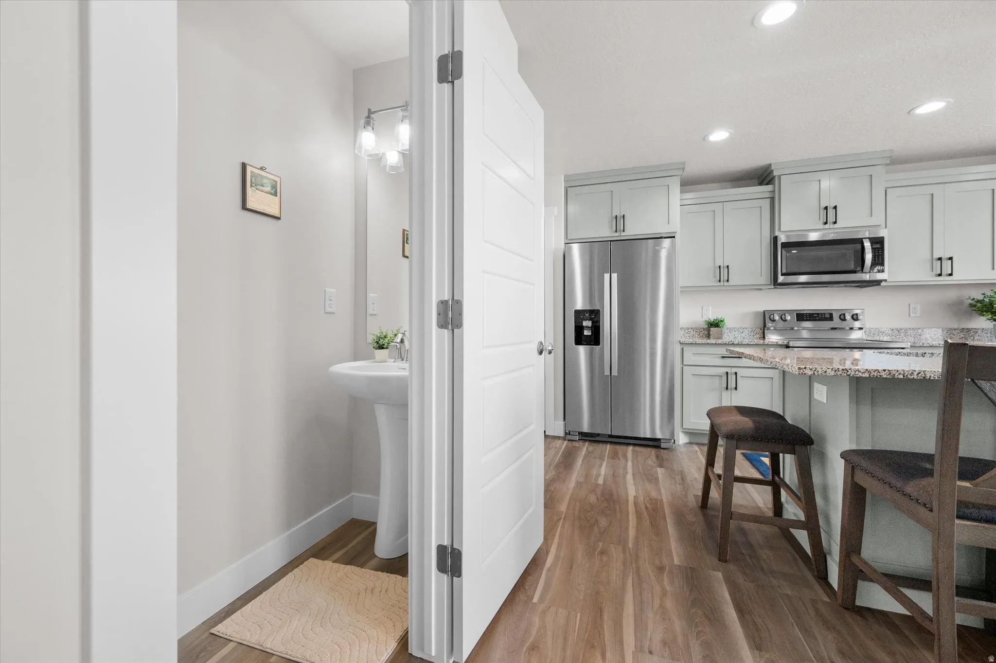 Kitchen with stainless steel appliances, light stone countertops, light wood-style floors, a breakfast bar, and recessed lighting