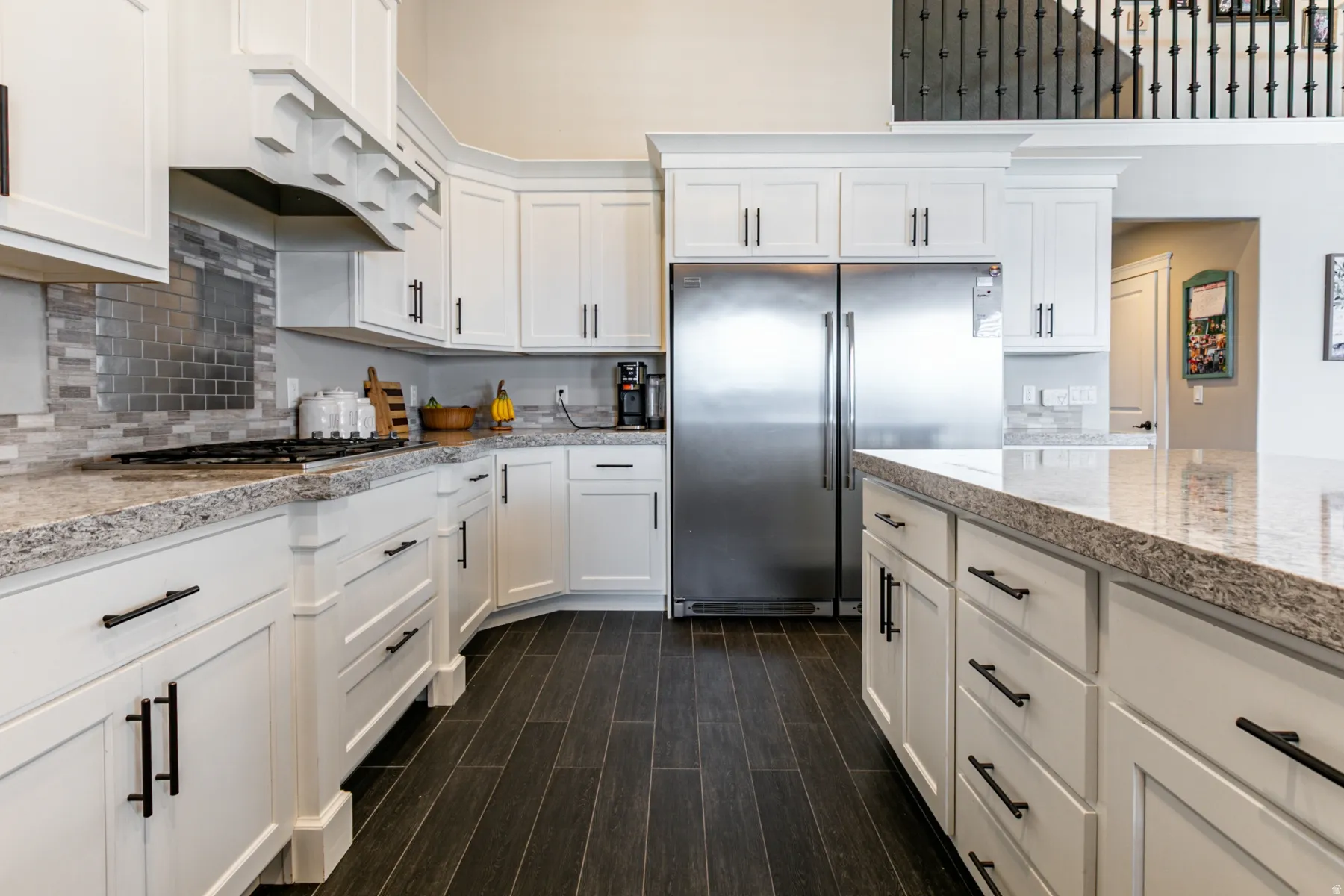 Kitchen featuring stainless steel refrigerator, white cabinetry, dark wood-style floors, and light stone countertops