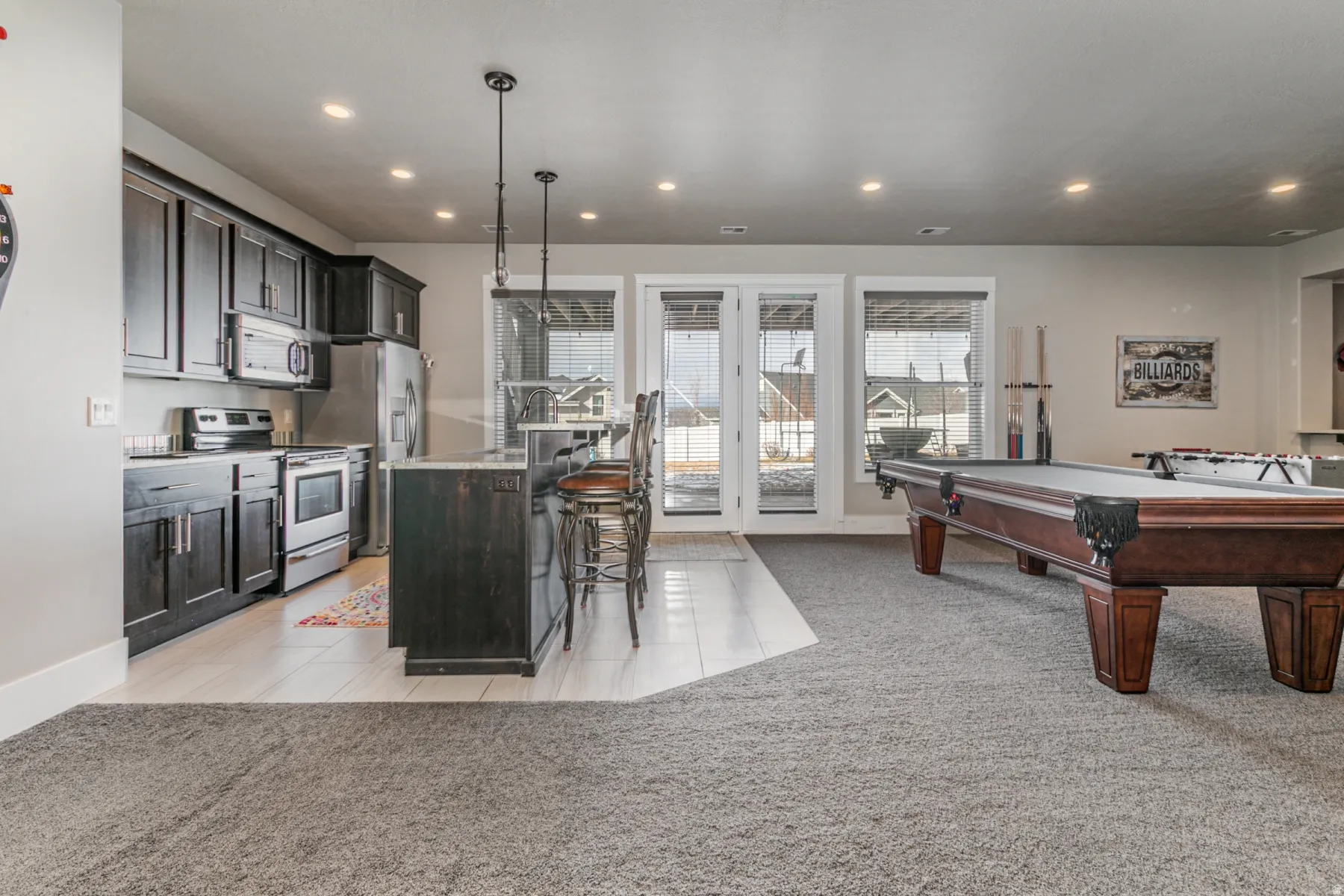Kitchen featuring light tile patterned floors, stainless steel appliances, light carpet, hanging light fixtures, and a center island with sink