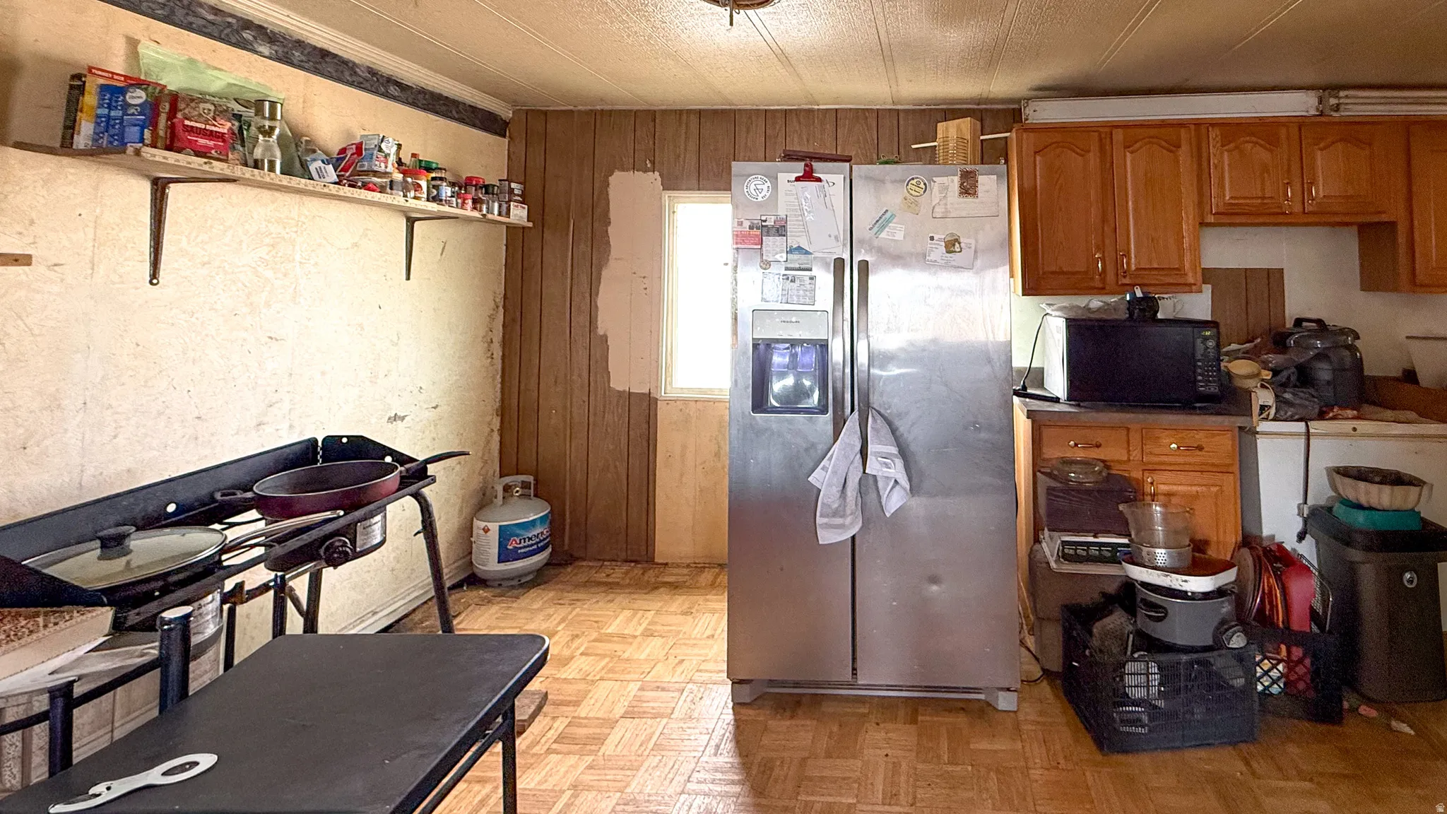 Kitchen with wood finish cabinets, stainless steel refrigerator with ice dispenser, wood walls, parquet flooring, and black microwave
