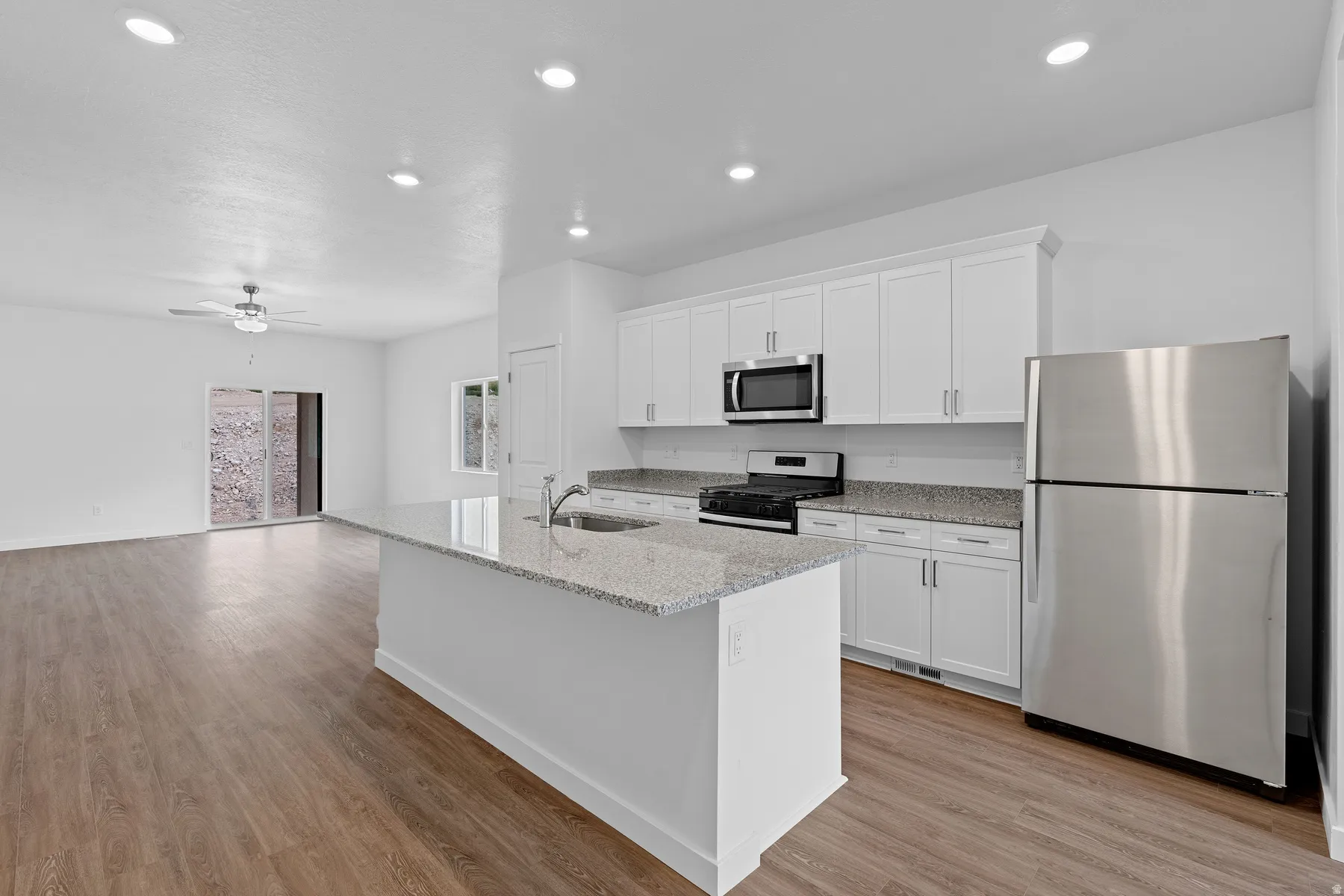 Kitchen featuring stainless steel appliances, light stone counters, white cabinets, a ceiling fan, and light wood-type flooring
