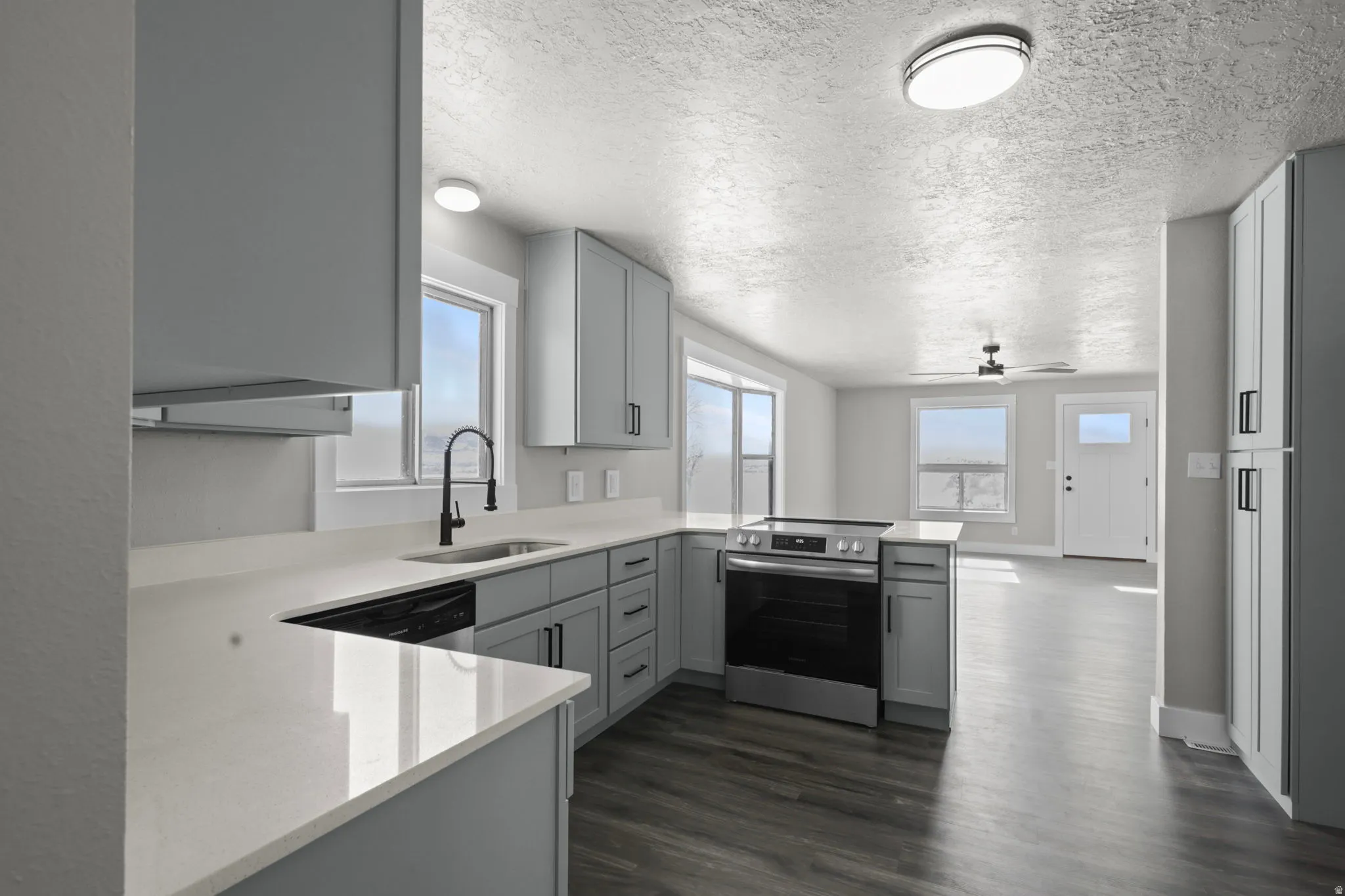 Kitchen with a peninsula, stainless steel appliances, gray cabinetry, light stone counters, and a textured ceiling