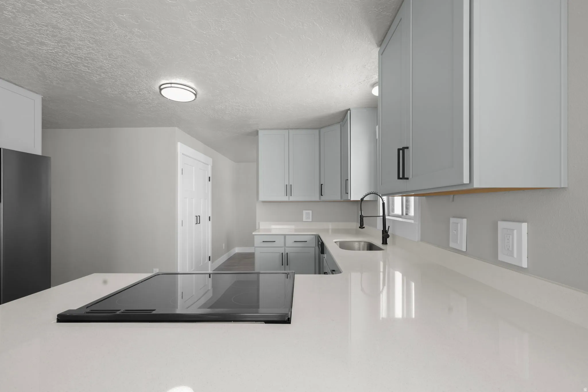 Kitchen featuring black electric stovetop, light stone counters, freestanding refrigerator, a textured ceiling, and a peninsula
