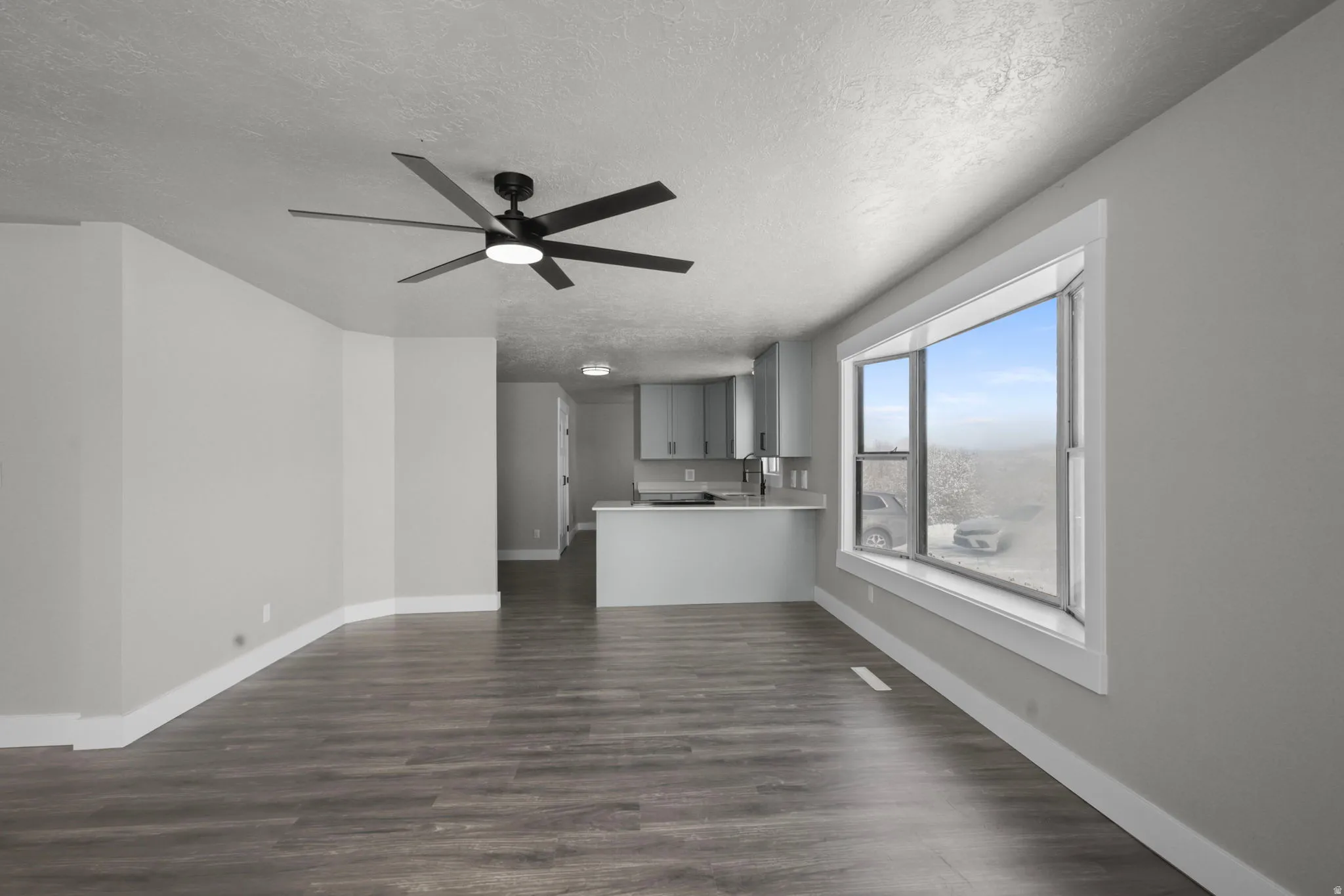 Unfurnished living room with dark wood-style floors, a ceiling fan, and a textured ceiling