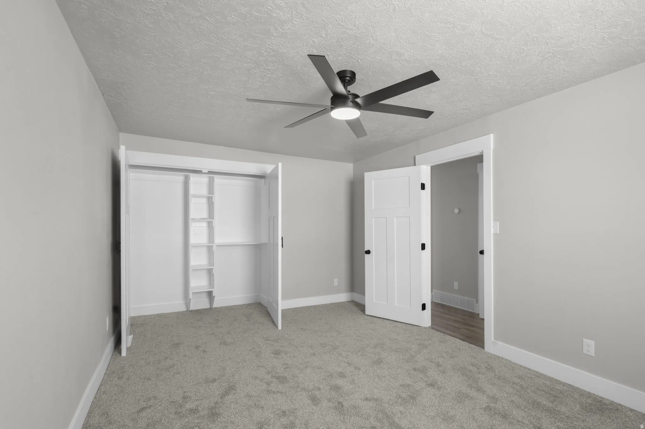 Unfurnished bedroom with light carpet, ceiling fan, a textured ceiling, and a closet