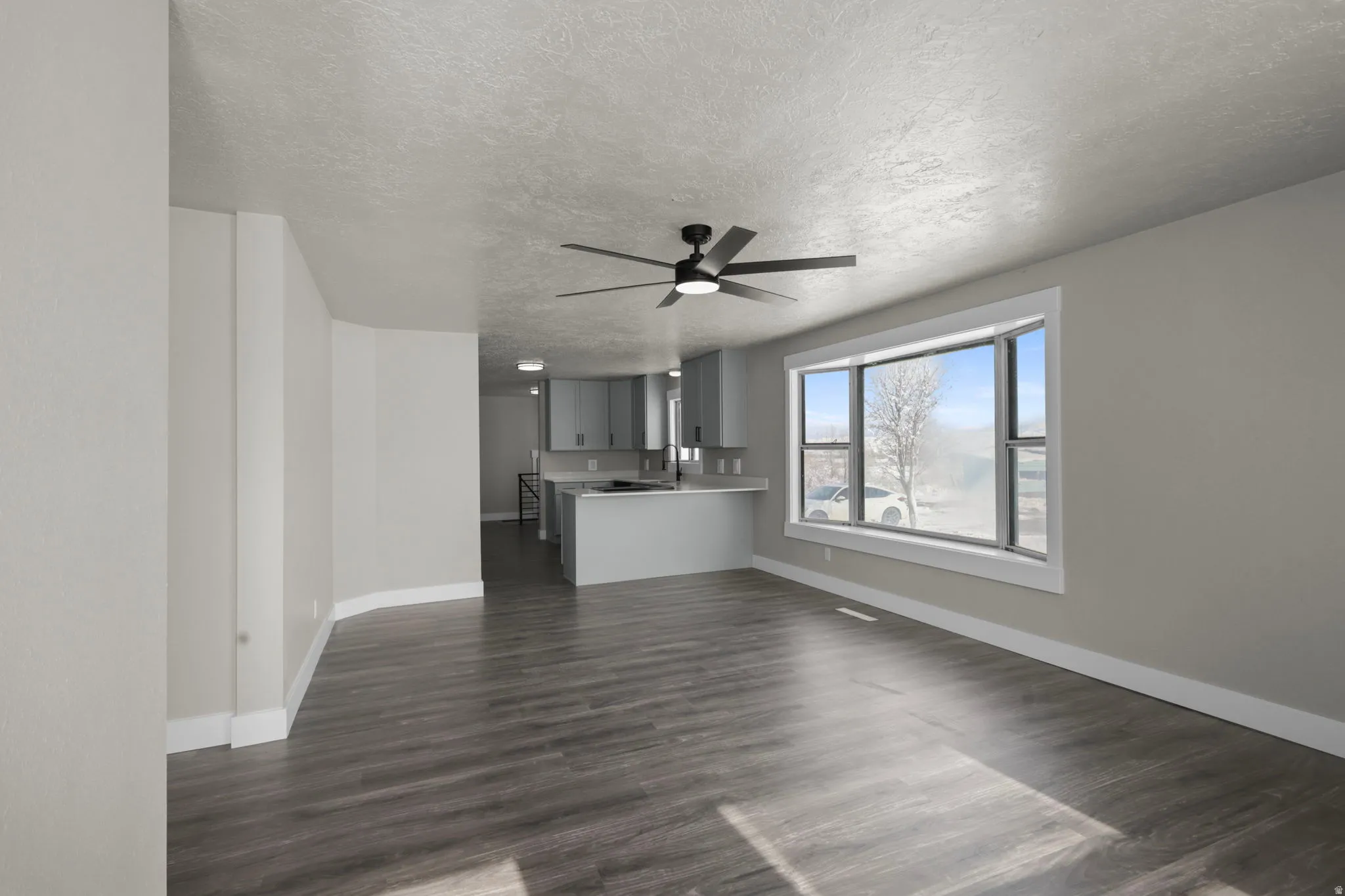 Unfurnished living room with dark wood-type flooring, ceiling fan, and a textured ceiling