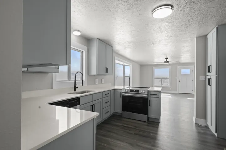 Kitchen with a peninsula, stainless steel appliances, gray cabinetry, light stone counters, and a textured ceiling