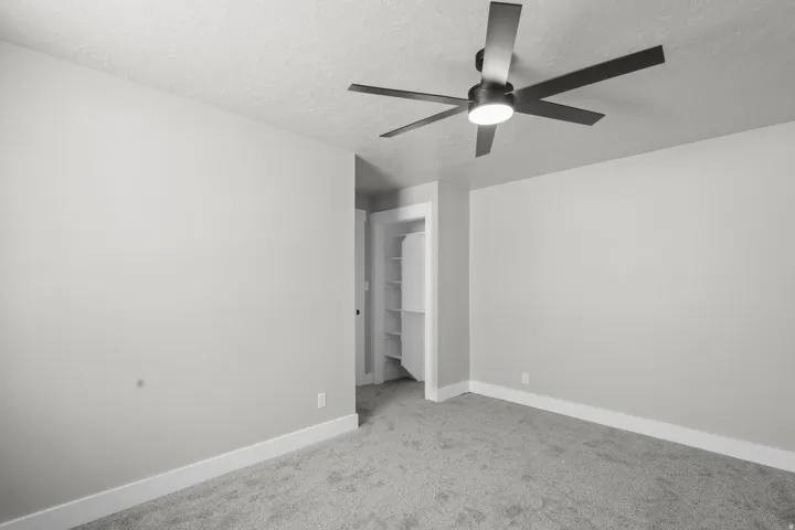 Unfurnished bedroom featuring carpet, a spacious closet, a textured ceiling, and ceiling fan