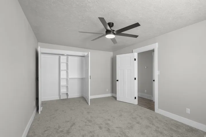 Unfurnished bedroom with light carpet, ceiling fan, a textured ceiling, and a closet