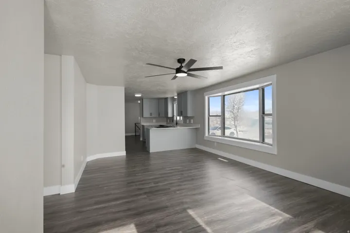 Unfurnished living room with dark wood-type flooring, ceiling fan, and a textured ceiling