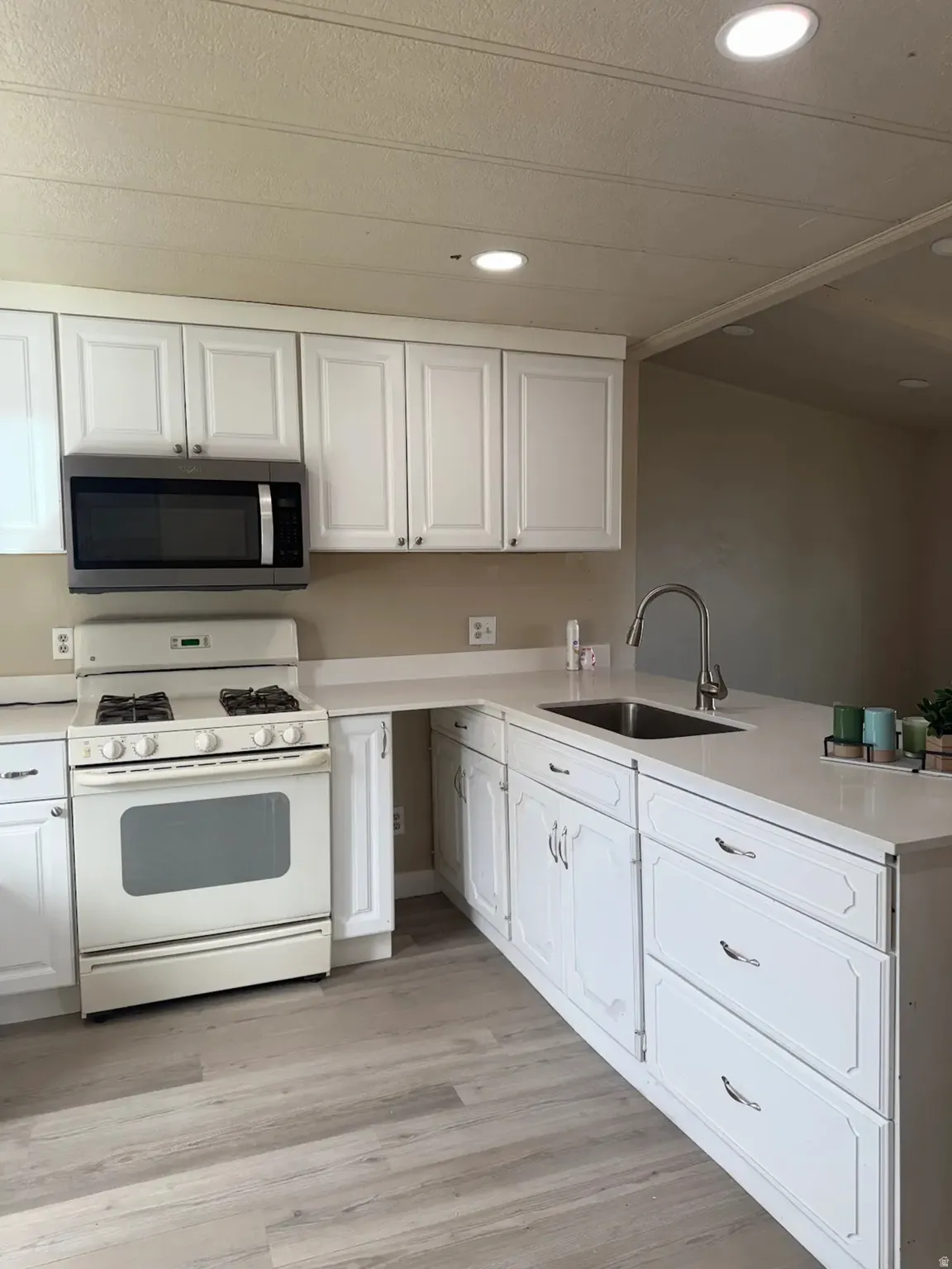 Kitchen with white gas range oven, stainless steel microwave, white cabinetry, recessed lighting, and light wood-style flooring