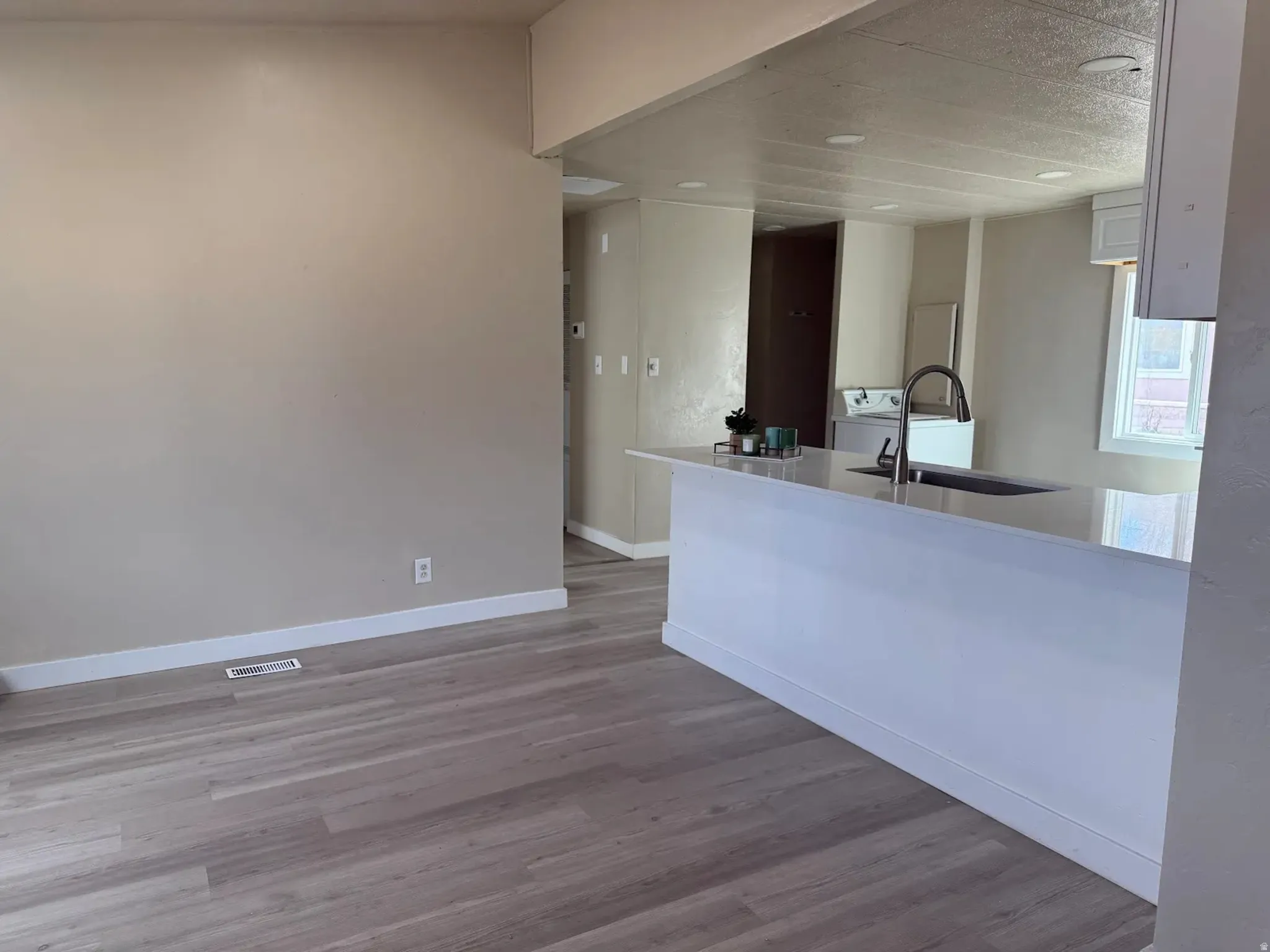 Kitchen with white cabinets, light wood finished floors, light stone countertops, a peninsula, and washer / dryer