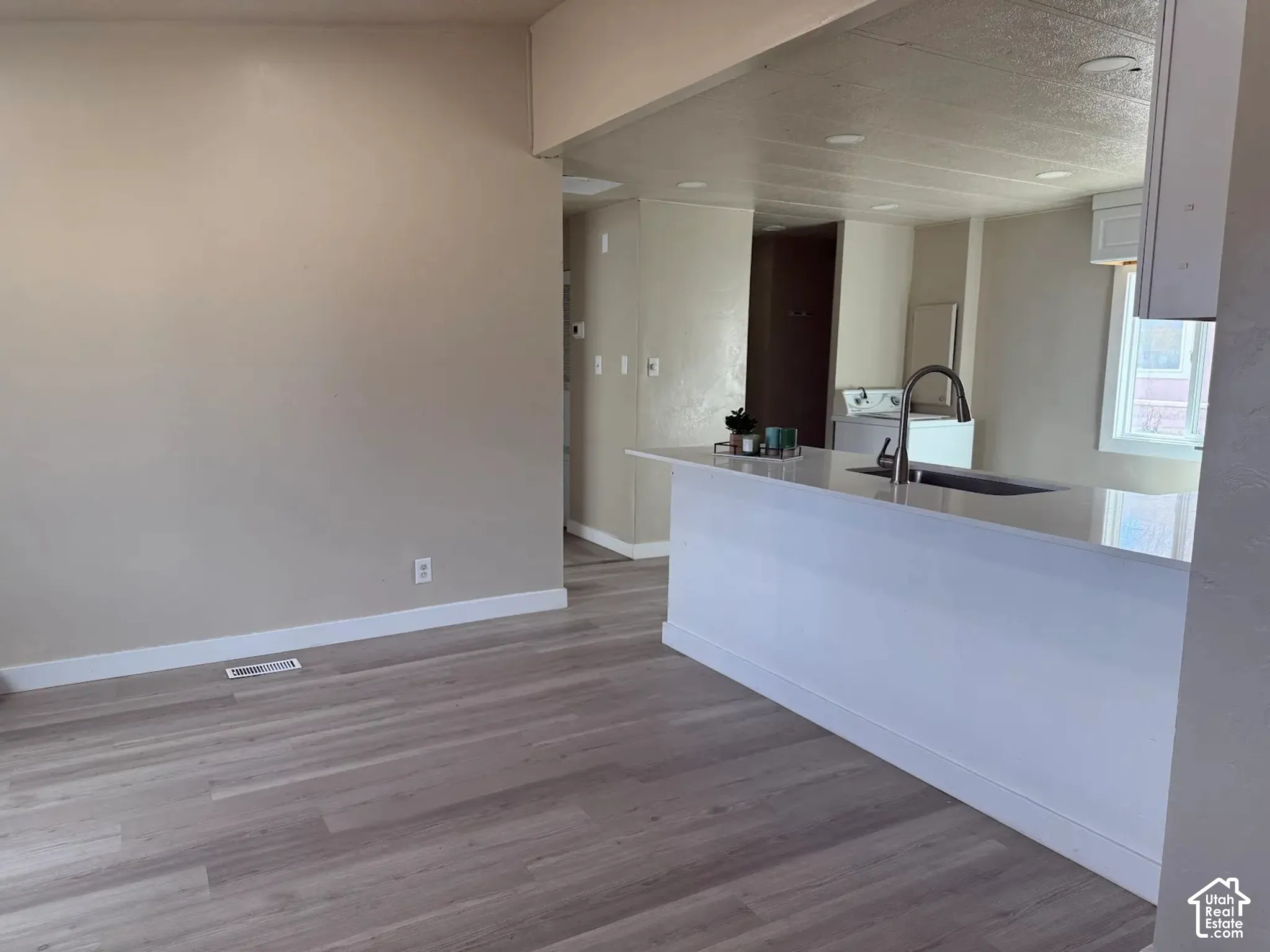 Kitchen with white cabinets, light wood finished floors, light stone countertops, a peninsula, and washer / dryer