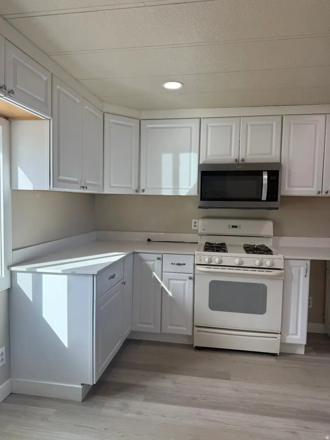 Kitchen with gas range gas stove, stainless steel microwave, light countertops, white cabinets, and recessed lighting