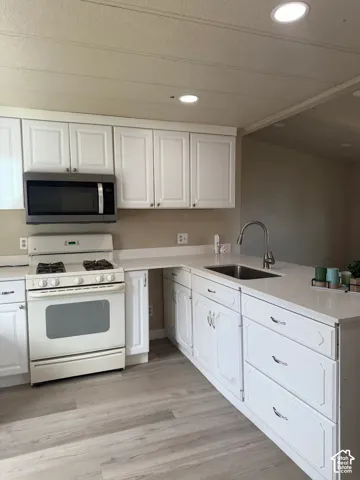 Kitchen with white gas range oven, stainless steel microwave, white cabinetry, recessed lighting, and light wood-style flooring