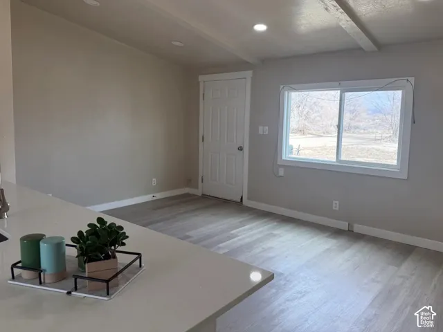 Unfurnished living room with light wood-type flooring, beam ceiling, and recessed lighting