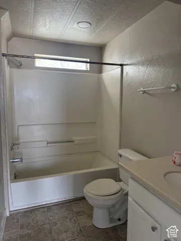 Full bathroom with a textured wall, vanity, shower / washtub combination, and a textured ceiling
