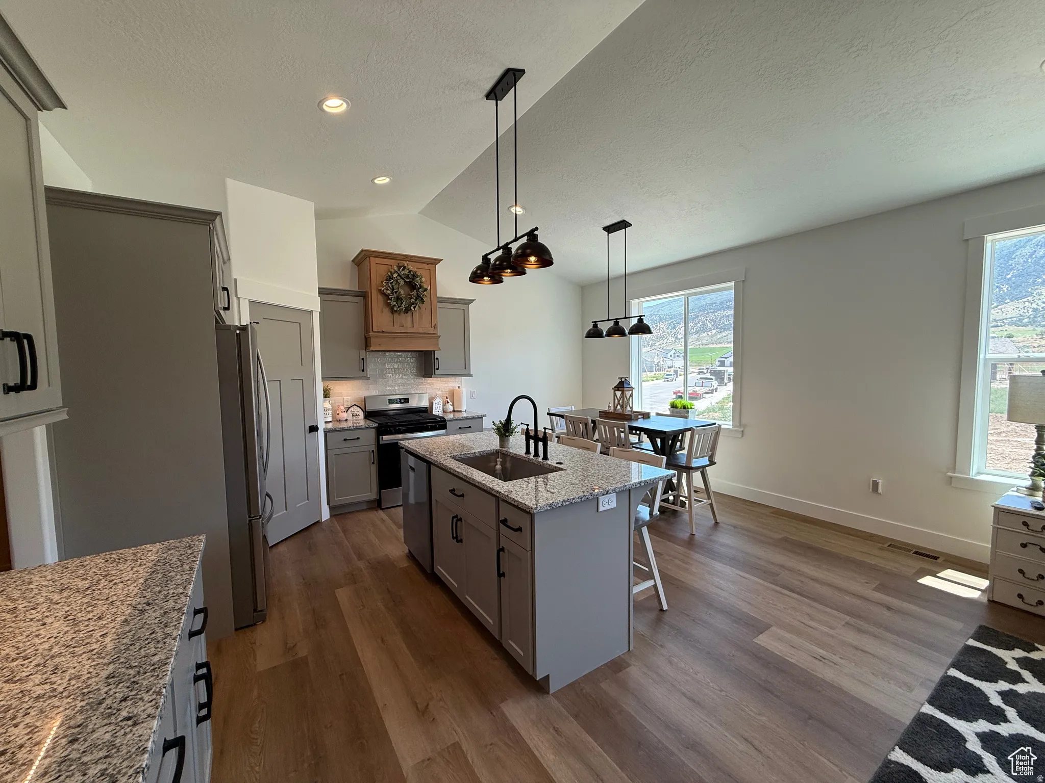 Kitchen with light stone countertops, hanging light fixtures, gray cabinets, dark wood-type flooring, and a center island with sink