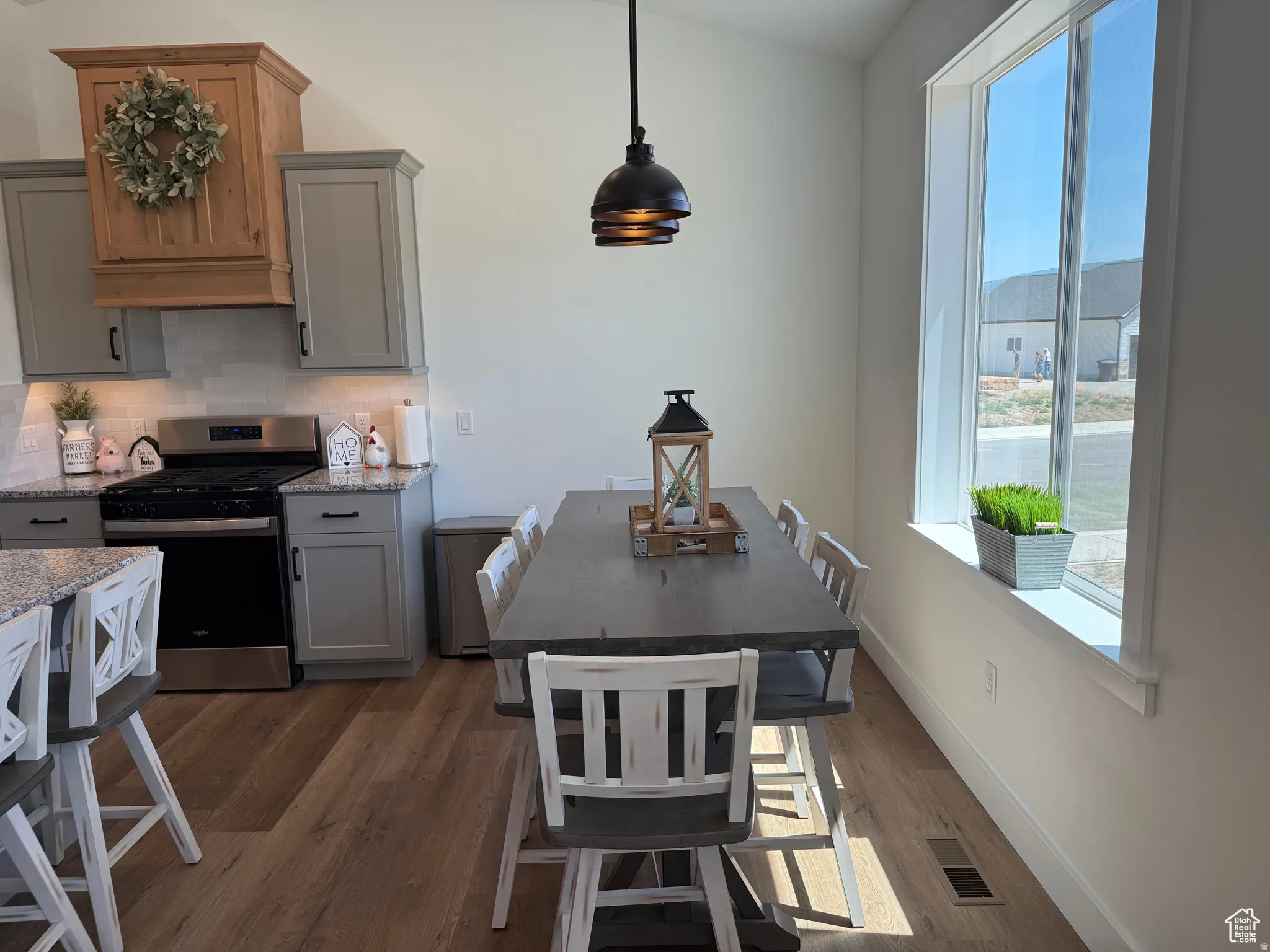 Kitchen with gray cabinets, gas stove, dark wood-type flooring, light stone countertops, and pendant lighting