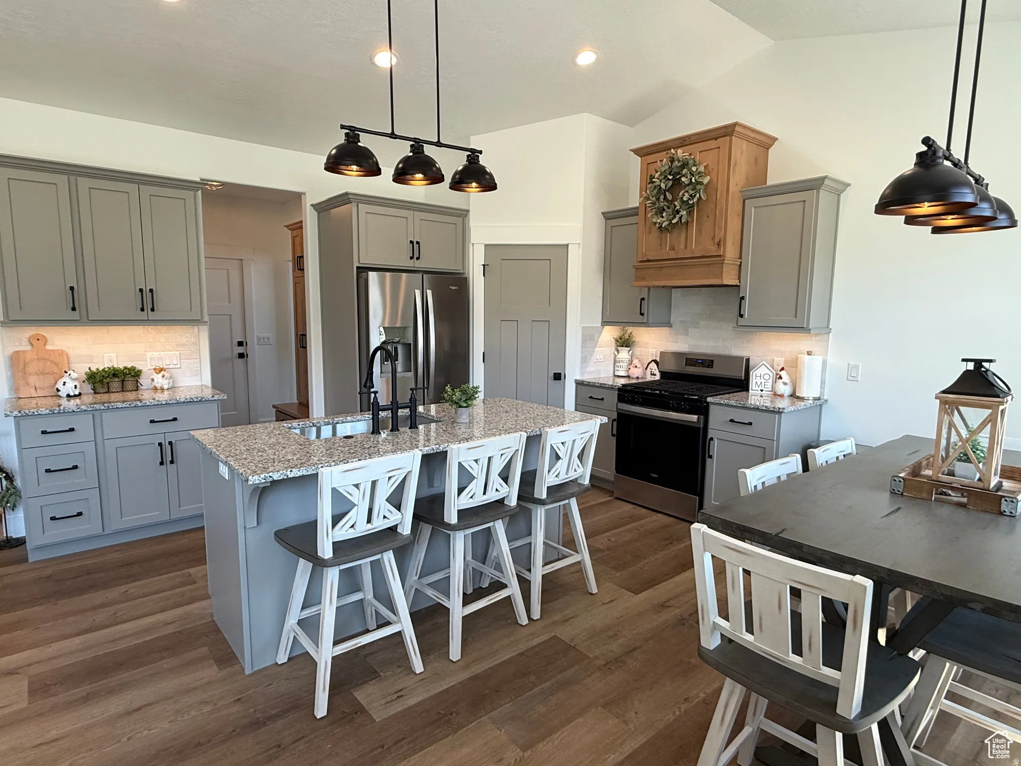 Kitchen with gray cabinetry, a breakfast bar, decorative backsplash, light stone countertops, and lofted ceiling
